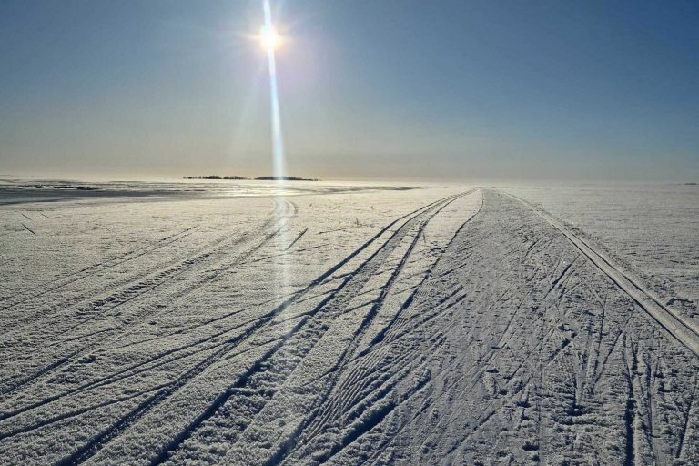 Hiihtoreitti jäällä, aurinko paistaa horisontissa.